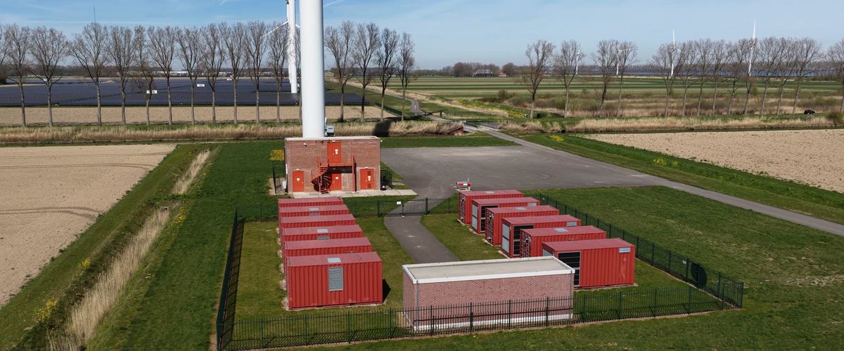Accumulo a batterie in container accanto a una turbina eolica, in campagna